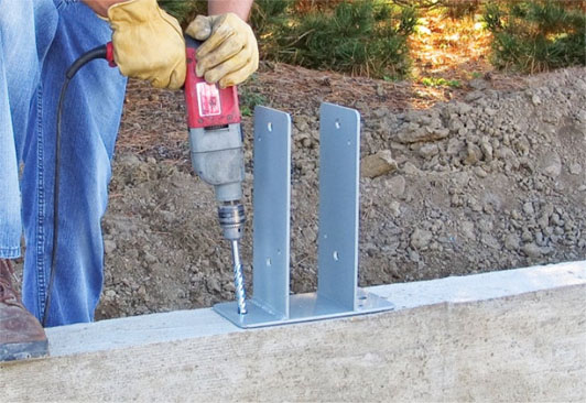 Construction worker installing Sturi-Wall® bracket with drill on concrete foundation